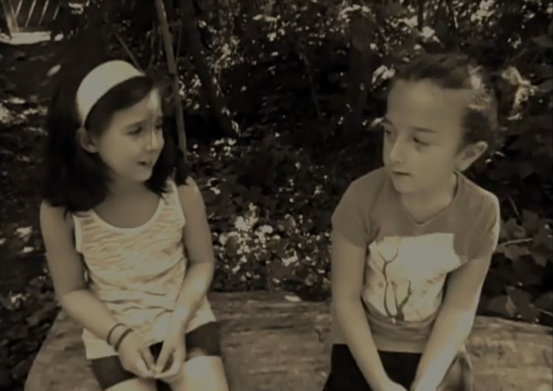 Sepia still from Laynastasia (2011, Marcel Potvin): two cousins sit side by side on a log in the woods, talking