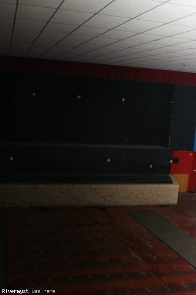 The bare front wall of an auditorium where the screen once hung, above a low brick stage and a red-patterned floor.