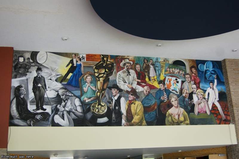 A long painted mural above the lobby showing film legends — Charlie Chaplin, a giant Oscar statue, John Wayne, Elvis, Marilyn Monroe, Darth Vader and John Travolta in his white Saturday Night Fever suit.