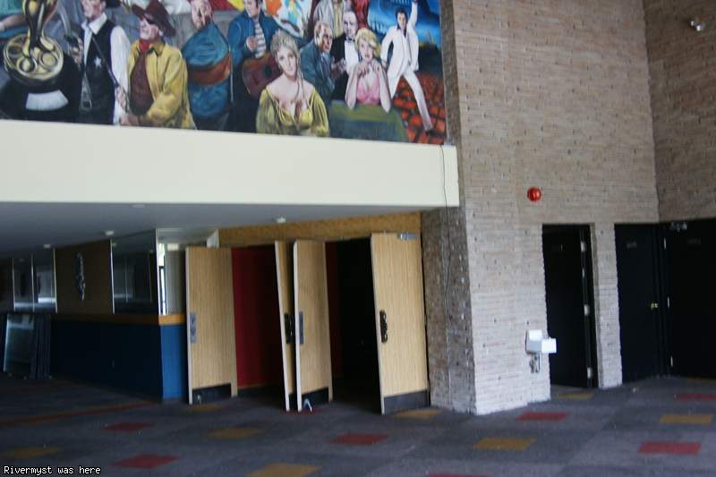 The lobby under the mural, with wooden doors standing open, tall brick pillars and a dark carpet with red and yellow squares.